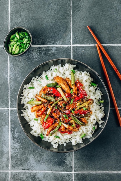 Stir fry with chicken meat vegetables and rice in black bowl on dark tiled stone background