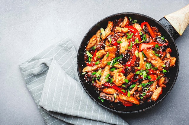 사진 프라이팬 아시아 요리 접시에 닭고기 붉은 파프리카 버섯과 향신료를 넣고 볶습니다. 회색 주방 테이블 배경 평면도 복사 공간