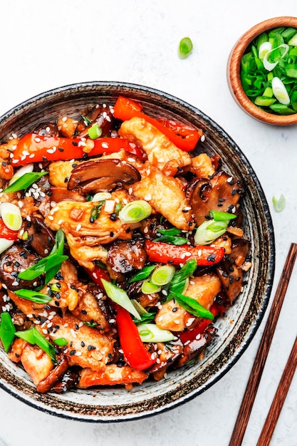 Stir fry with turkey fillet red paprika mushrooms green chives and sesame seeds in bowl Asian cuisine dish White kitchen table background top view