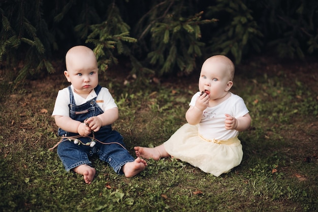 Stock foto van schattige kleine baby's zittend op het gras in het bos. Broertje en zusje bessen eten zittend op groen gras in het bos.