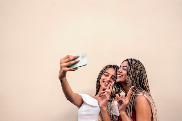 Stock photo of attractive african american sisters with cool braids smiling and taking selfie in the street.