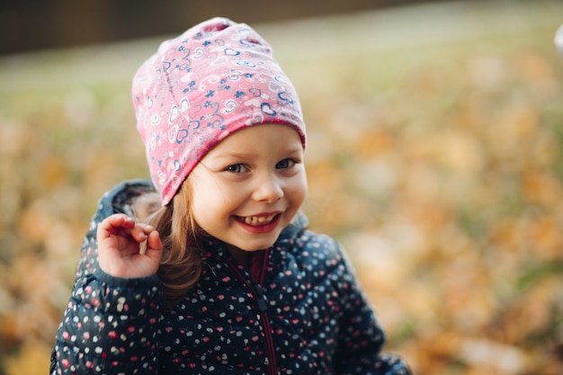 ピンクの印刷された帽子と暗い印刷された冬のジャケットを笑顔で手を振っているかわいい少女のストックフォト。