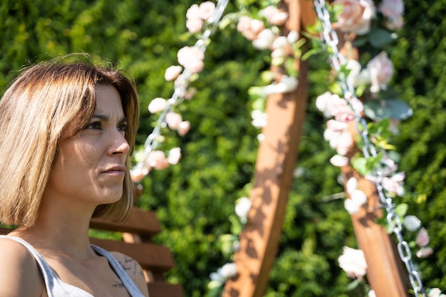 Stock photo of a detail of the face of a girl sitting on a wooden swing decorated with flowers in a garden. Lifestyle