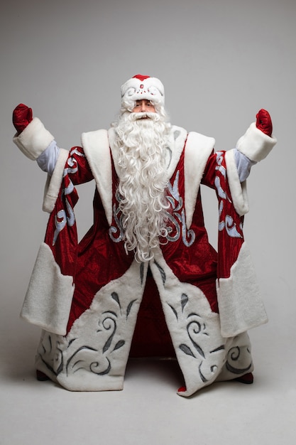 Photo stock photo of a father frost with long white beard in traditional red costume with hat and mittens holding inflatable air balloon in right hand raised up.