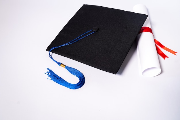 Stock photo of a graduation cap mortar board and diploma\
certificate isolated on white background with negative copy space\
to add text. graduation hat with diploma on table against white\
background