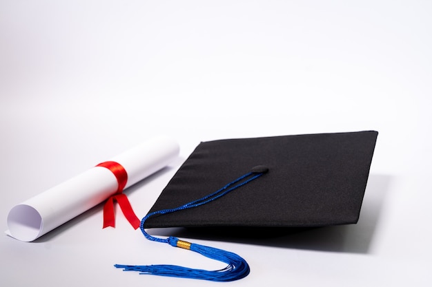 Stock photo of a graduation cap mortar board and diploma certificate isolated on white background with negative copy space to add text. Graduation hat with diploma on table against white background