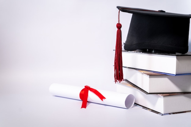 テキストを追加するためのネガコピースペースで白い背景に分離された卒業帽のモルタルボードと卒業証書のストックフォト。白い背景のテーブルに卒業証書と卒業帽子