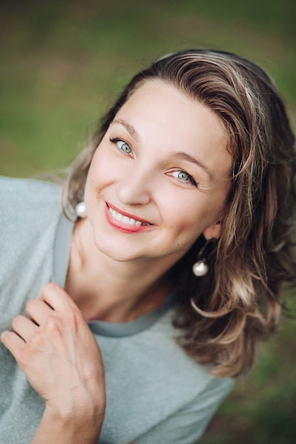 Stock photo headshot of an attractive young woman with dyed middle length hair with red lips and earrings smiling at camera with happiness. Blurred background.