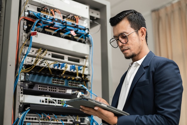 Stock photo of a young network technician holding tablet
working to connecting network cables in server cabinet in network
server room. it engineer working in network server room