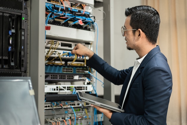 Stock photo of a young network technician holding tablet
working to connecting network cables in server cabinet in network
server room. it engineer working in network server room