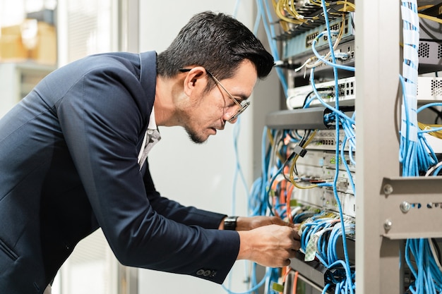 Stock photo of a young network technician holding tablet working to connecting network cables in server cabinet in network server room. IT engineer working in network server room