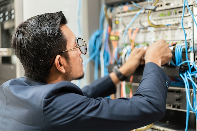 Stock photo of a young network technician holding tablet\
working to connecting network cables in server cabinet in network\
server room. it engineer working in network server room