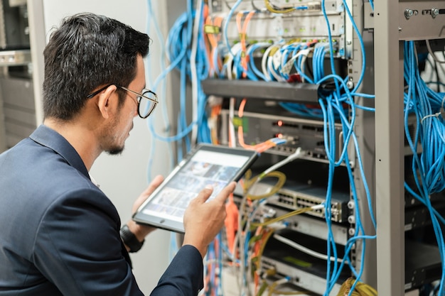 Foto di stock di un giovane tecnico di rete che tiene in mano un tablet che lavora per collegare i cavi di rete nell'armadio del server nella stanza del server di rete. ingegnere it che lavora nella sala server di rete