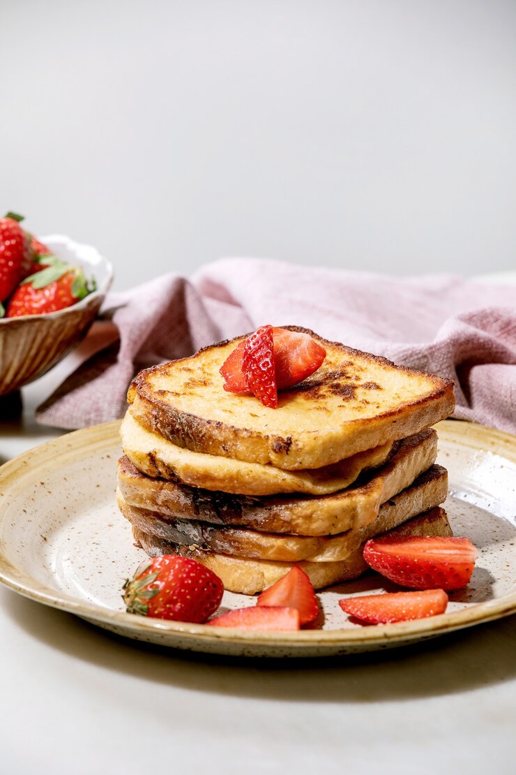 Photo stockpile of french toasts with fresh strawberries on ceramic plate and pink cloth napkin over white table