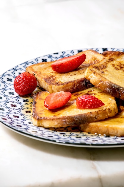 Stockpile of french toasts with fresh strawberries and maple syrup on ceramic plate on white marble table. Close up