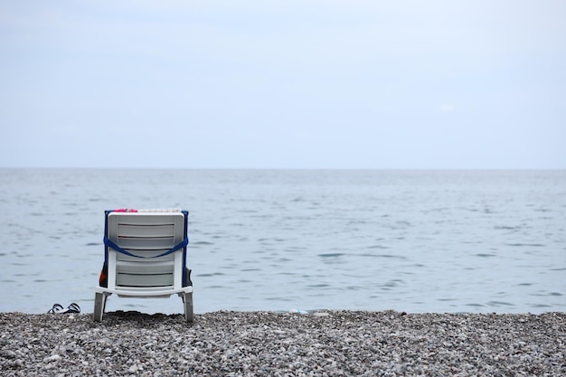 Stoel op oever van kiezelstenen met de zee en het strand