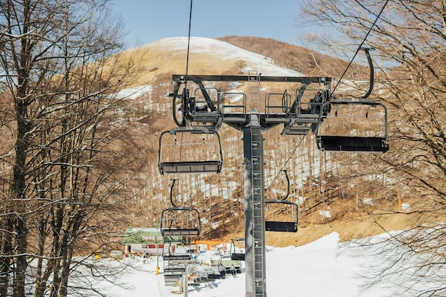 Stoeltjeslift, besneeuwde skipiste in bergen en blauwe lucht in de winter.