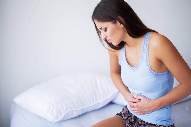 Photo stomach pain. unhealthy young woman with stomachache leaning on the bed at home