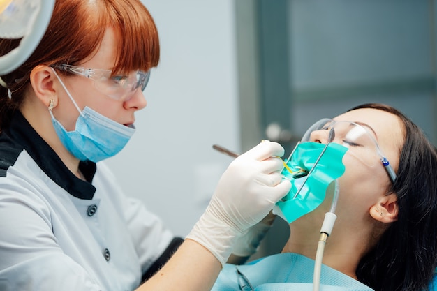 Stomatologist is using medical instruments and making treatment to female patient in safety glasses.