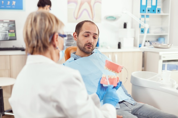 Infermiera stomatologo che spiega all'uomo malato l'intervento chirurgico utilizzando il modello in gesso del dentista dentista che tiene in mano un modello di scheletro di denti, campione di mascella umana che parla