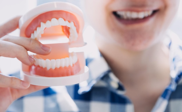 Stomatology concept partial portrait of girl with strong white teeth looking at camera and smiling fingers near face Closeup of young woman at dentist's studio indoors