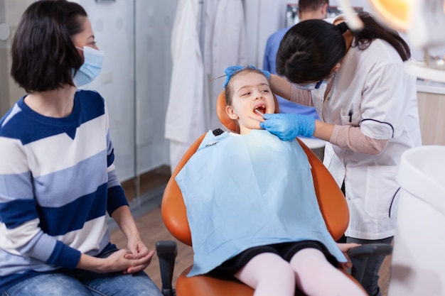 Stomatology doctor using dental mirror in the course of little girl examination. Dentistry specialist during child cavity consultation in stomatology office using modern technology.