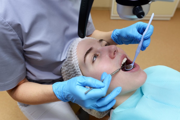 Stomatoloog die tanden van de patiënt onderzoekt met behulp van professionele tandheelkundige microscoop tandarts die cariës voorkomt met behulp van restauratie-instrumenten cliënt liggend op tandartsstoel
