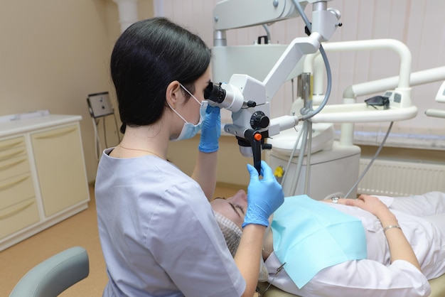 Stomatoloog die tanden van patiënt onderzoekt met behulp van professionele tandheelkundige microscoop Tandarts die cariës voorkomt met behulp van restauratie-instrumenten Cliënt liggend op tandartsstoel
