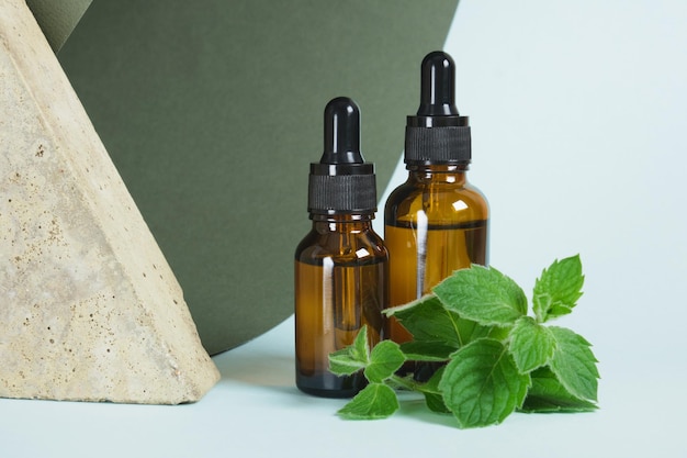 Stone, amber glass dropper bottles and mint leaves, peppermint oil in a bottle with pipette, the use of peppermint oil in aromatherapy and cosmetics mock up