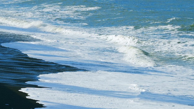 Каменный пляж с мелкими камешками, омываемый мелкими пенообразными волнами, чистая вода у моря, спокойная.