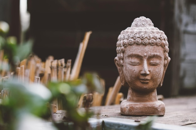 Stone bust of Buddha on black wooden desk with blurred background standing on the wooden floor