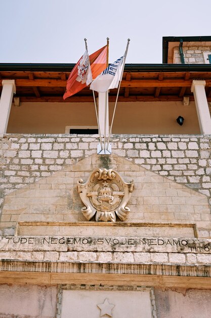 Foto stampo intagliato in pietra e bandiere sventolate sui pali sopra la vecchia porta marittima di kotor montenegro