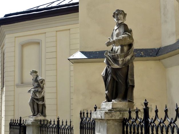 Stone figure of a man against the background of an old wall on a column of an iron fence