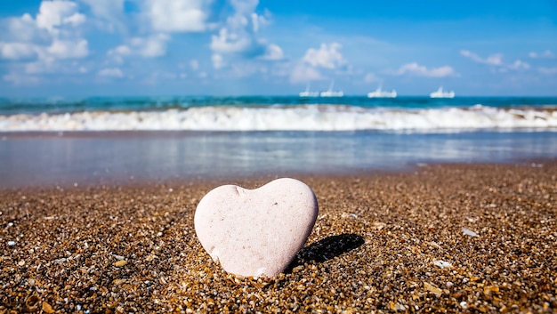 여름 해변에 서있는 돌의 심장 모양의 모래 사랑 개념