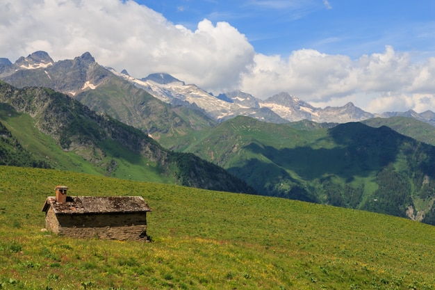 Capanna di pietra in campo verde con montagne e nuvole sullo sfondo