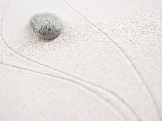 線が描かれた砂の表面に石が置かれています。