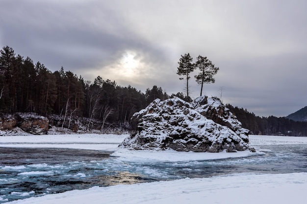 Stone island with pine trees in the middle of a freezing river on a winter cloudy day