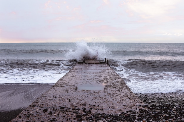 Stone pier on the coastline with waves and horizon line