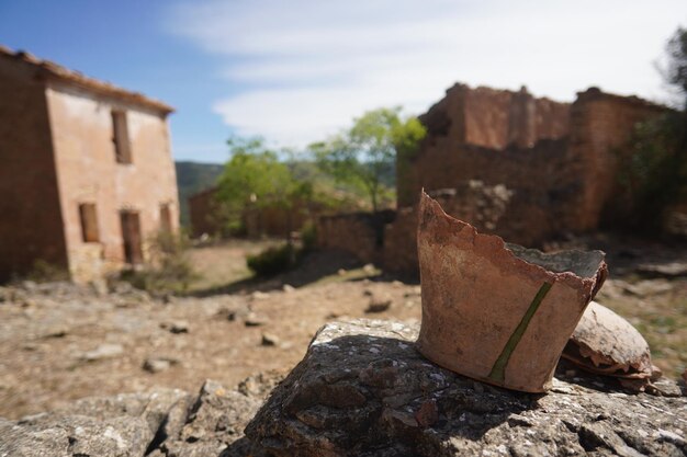 A stone pot sits on a rock in front of a house with a tree in the background.