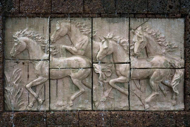 Каменная скульптура лошадей на стене с водопадом