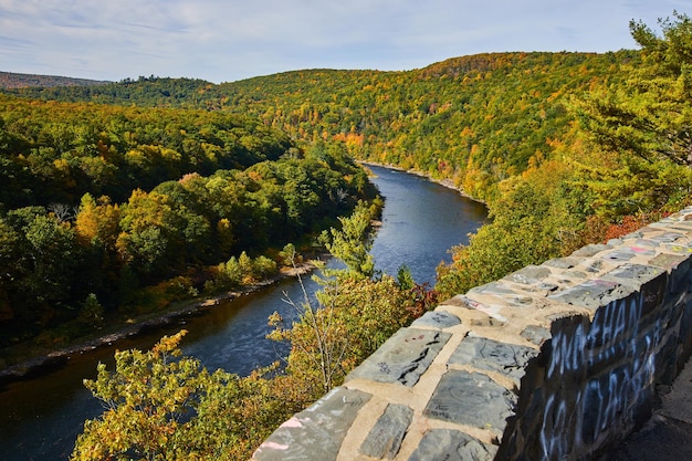 Stone wall along overlook above Delaware River going through early fall forest