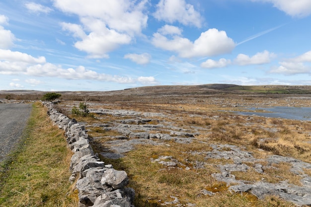 A stone wall in the grass with a blue sky and clouds in the background