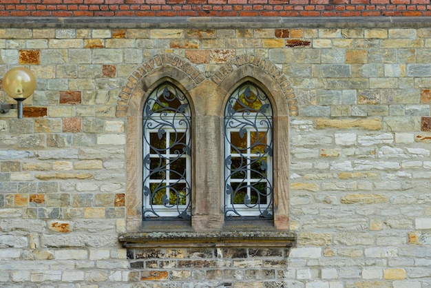 Stone wall of an old building with two arched windows Windows are closed with decorate metal grid