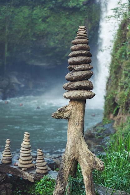 Stones of different sizes are stacked one on top of the other against the backdrop of a waterfall.