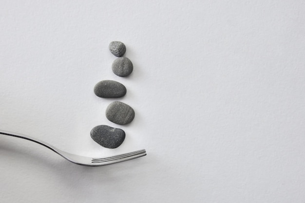 Stones on a fork, a symbol of heavy, unhealthy food on a gray background