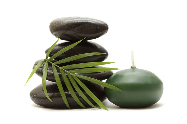 Stones, green leaves and a candle on a white background