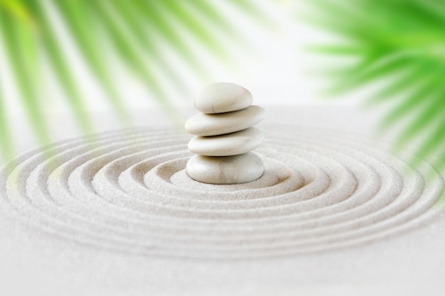 Photo stones pile in the sand behind palm leaves. zen japanese garden