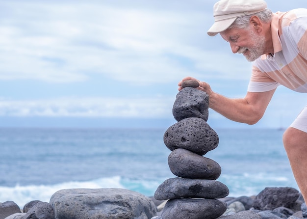 Torre di pietre sulla costa del mare nella natura spiaggia dell'oceano torre di sei ciottoli uomo sorridente caucasico mettere l'ultimo pezzo concetto di equilibrio e armonia