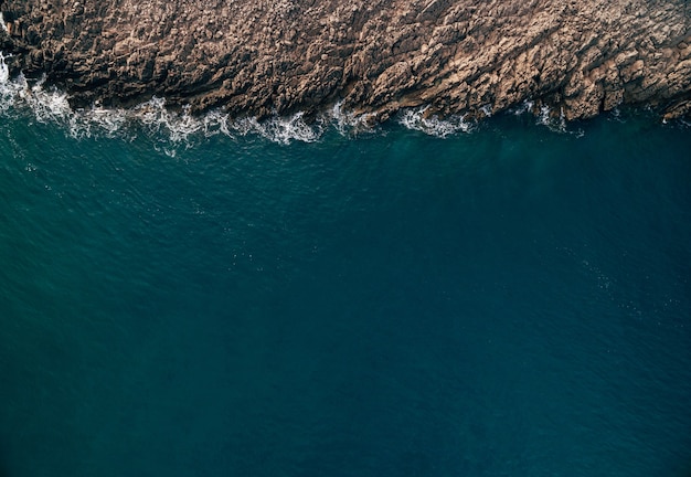 Stones turquoise waves and sea foam from above Atlantic ocean coastline with rocks aerial view