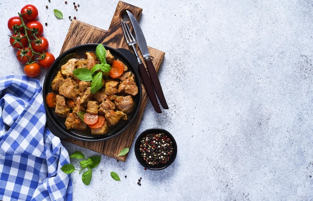 Stoofpot met kruiden en wortelen stoofpot in een gietijzeren pan op een betonnen ondergrond met tomaten